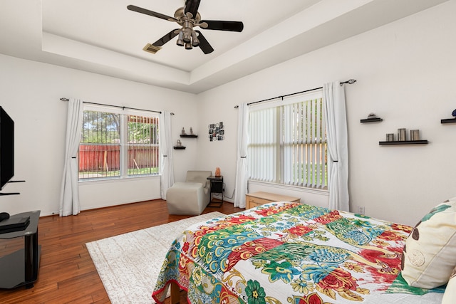 25807 Oakridge Forest Ln, Spring, TX 77386 - bedroom featuring multiple windows, wood finished floors, a tray ceiling, and a ceiling fan