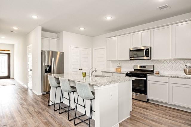 23242 Spring Genesis Ln, Katy, TX 77493 - kitchen with stainless steel appliances, a center island with sink, light stone countertops, light wood-style floors, and tasteful backsplash
