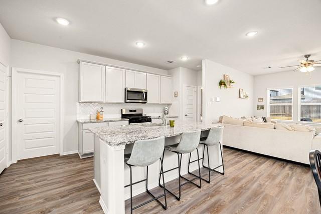 23242 Spring Genesis Ln, Katy, TX 77493 - kitchen featuring stainless steel appliances, open floor plan, a kitchen bar, wood finished floors, and light stone counters