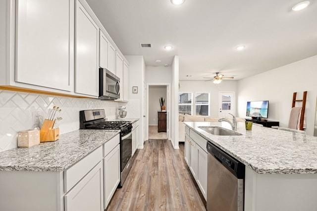 23242 Spring Genesis Ln, Katy, TX 77493 - kitchen with appliances with stainless steel finishes, light wood-style floors, a ceiling fan, decorative backsplash, and white cabinetry