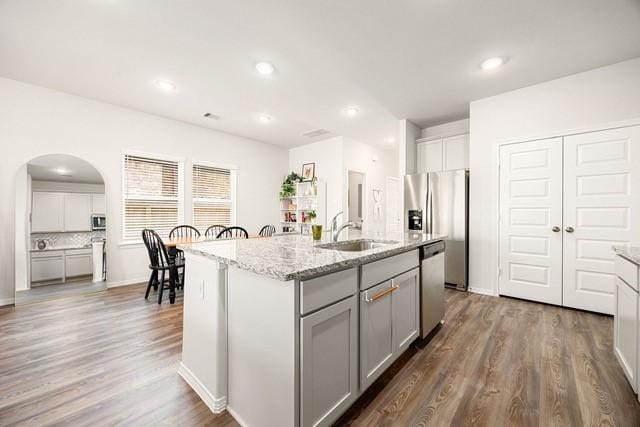 23242 Spring Genesis Ln, Katy, TX 77493 - kitchen featuring appliances with stainless steel finishes, gray cabinets, wood finished floors, light stone counters, and arched walkways