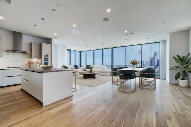 1711 Allen Pkwy Unit 2106, Houston, TX 77019 - kitchen with wall chimney range hood, modern cabinets, a wall of windows, light wood finished floors, and a center island