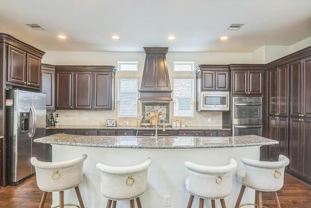 47 Chestnut Meadow Dr, Conroe, TX 77384 - kitchen featuring appliances with stainless steel finishes, a kitchen island with sink, a kitchen breakfast bar, dark brown cabinetry, and recessed lighting