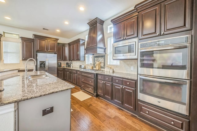 47 Chestnut Meadow Dr, Conroe, TX 77384 - kitchen with stainless steel appliances, premium range hood, dark brown cabinets, light wood-style floors, and recessed lighting