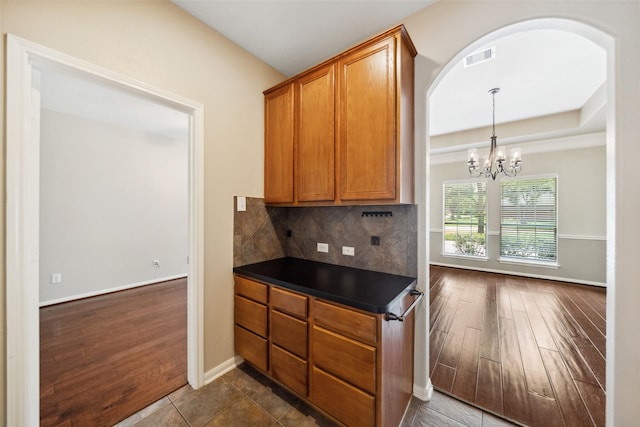 15331 Springhill Bend Ln, Cypress, TX 77429 - kitchen with dark countertops, brown cabinetry, arched walkways, dark wood-type flooring, and a chandelier