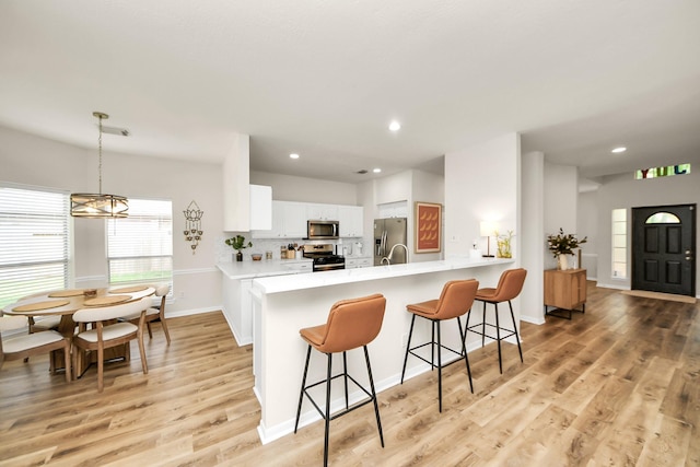 235 Cedar Elm Ln, Sugar Land, TX 77479 - kitchen with stainless steel appliances, a kitchen breakfast bar, a peninsula, white cabinets, and light wood-type flooring