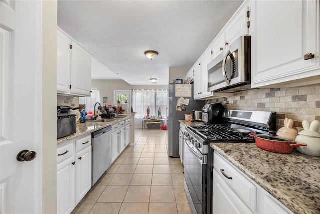 3825 Redbud Dr, La Porte, TX 77571 - kitchen with appliances with stainless steel finishes, white cabinets, tasteful backsplash, light tile patterned floors, and light stone countertops