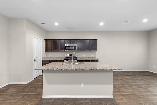 2431 Sutton Hollow Ct, Spring, TX 77373 - kitchen with appliances with stainless steel finishes, light stone countertops, an island with sink, dark wood-type flooring, and dark brown cabinetry