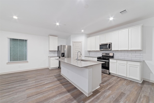 7002 Halifax Harvest Ln, Richmond, TX 77407 - kitchen with stainless steel appliances, tasteful backsplash, light wood-style floors, a center island with sink, and white cabinets