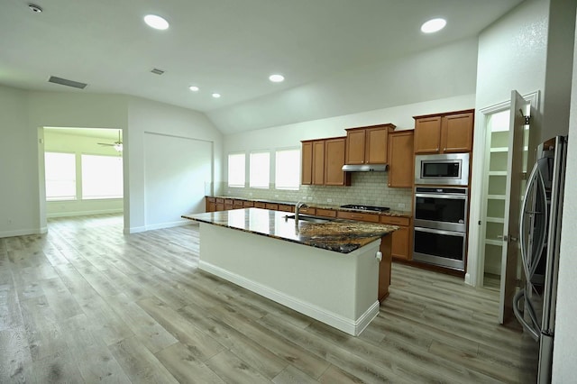 9002 Lacombe Ln, Tomball, TX 77375 - kitchen featuring stainless steel appliances, vaulted ceiling, brown cabinets, tasteful backsplash, and light wood finished floors