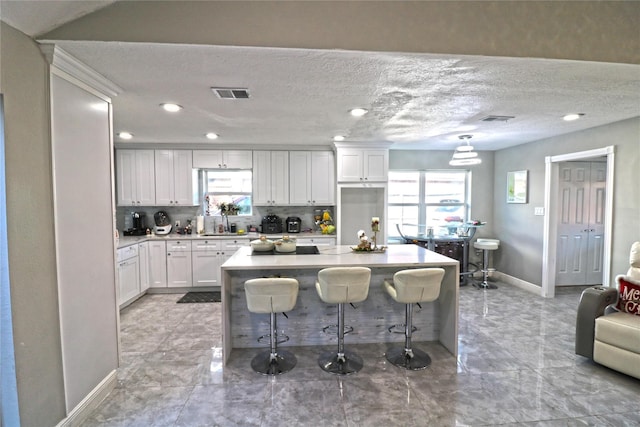 15902 Seven Springs Dr, Houston, TX 77084 - kitchen featuring a breakfast bar, white cabinetry, light countertops, decorative backsplash, and a center island