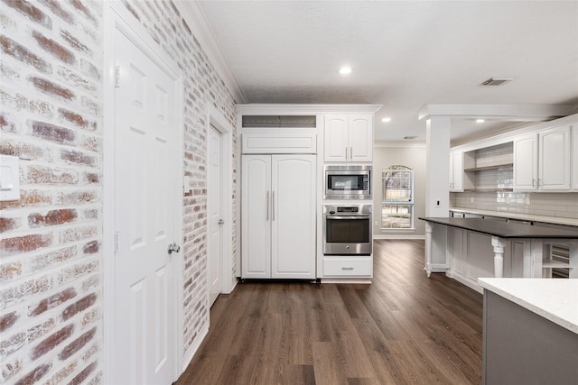 12014 Via Davinci Ln NW, Cypress, TX 77429 - kitchen with appliances with stainless steel finishes, dark wood-type flooring, white cabinetry, brick wall, and crown molding