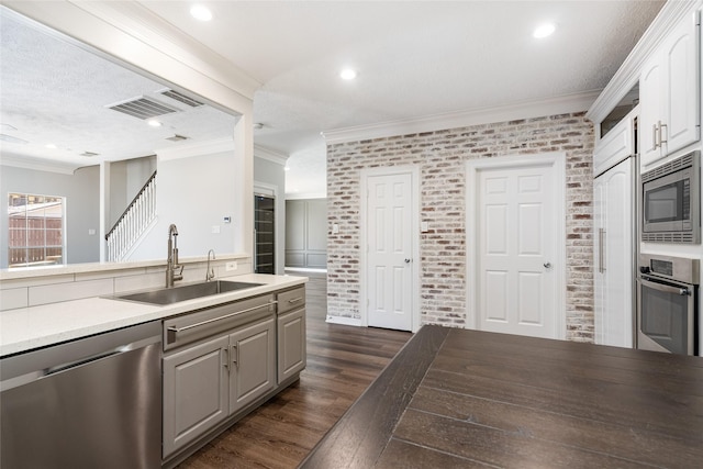 12014 Via Davinci Ln NW, Cypress, TX 77429 - kitchen with appliances with stainless steel finishes, dark wood finished floors, brick wall, recessed lighting, and ornamental molding