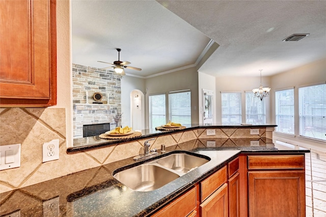 30 N Scribewood Cir, The Woodlands, TX 77382 - kitchen with brown cabinetry, tasteful backsplash, dark stone countertops, a stone fireplace, and pendant lighting