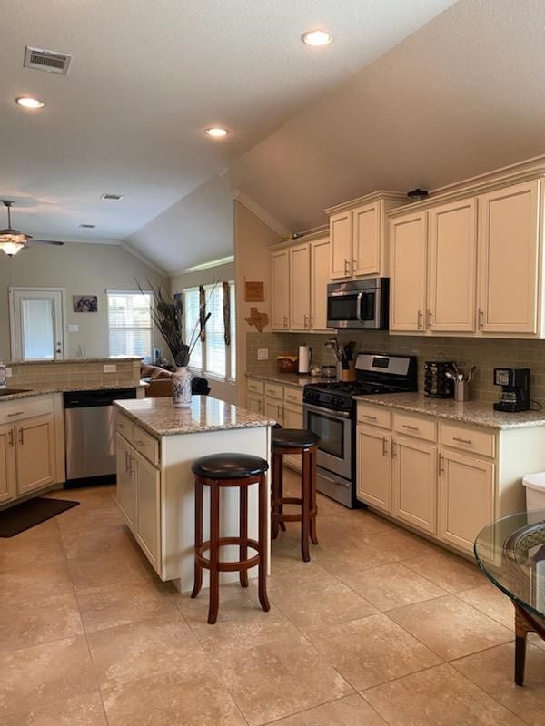 6727 Trinity Trail Ln, Richmond, TX 77469 - kitchen with stainless steel appliances, vaulted ceiling, backsplash, a kitchen island, and ceiling fan