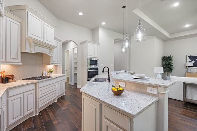 131 Evening Tide Ct, Conroe, TX 77318 - kitchen featuring arched walkways, stainless steel appliances, dark wood finished floors, decorative backsplash, and a center island with sink