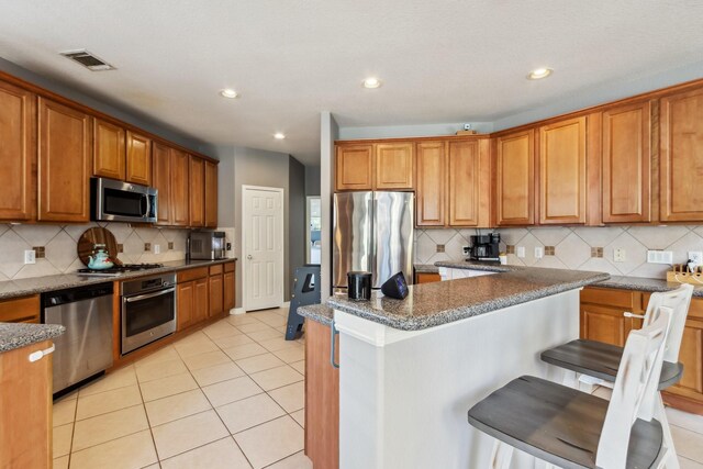 13518 Via Chianti Ln, Cypress, TX 77429 - kitchen featuring appliances with stainless steel finishes, brown cabinetry, backsplash, light tile patterned floors, and dark stone counters