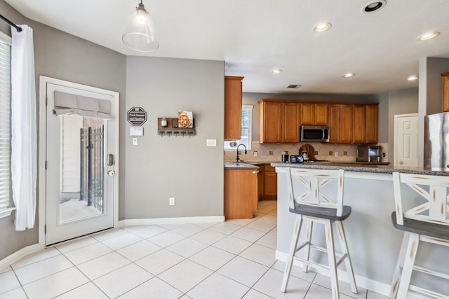 13518 Via Chianti Ln, Cypress, TX 77429 - kitchen with stainless steel microwave, a kitchen breakfast bar, tasteful backsplash, brown cabinets, and recessed lighting
