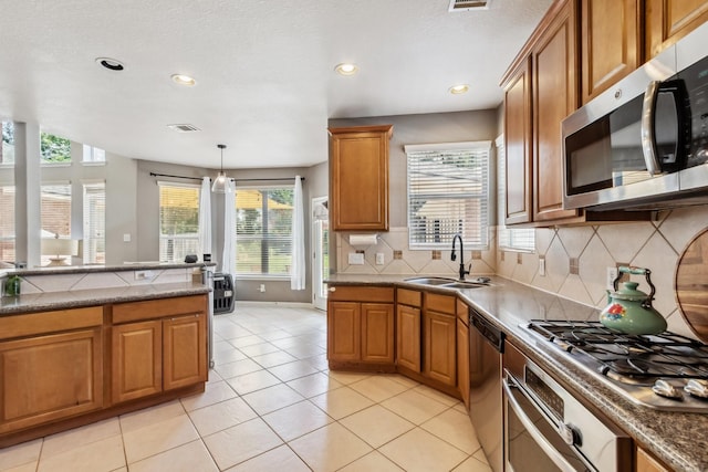 13518 Via Chianti Ln, Cypress, TX 77429 - kitchen with stainless steel appliances, brown cabinetry, backsplash, recessed lighting, and light tile patterned floors