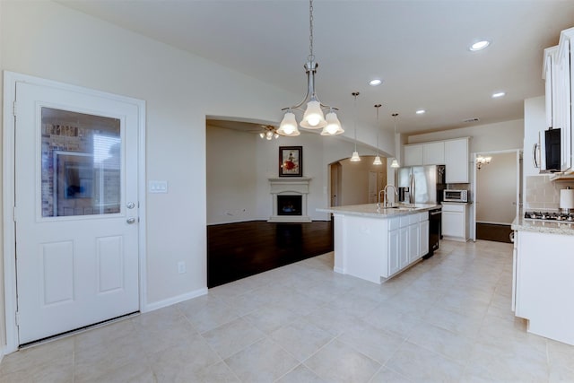 24014 Bluestem Ridge Ct, Katy, TX 77493 - kitchen featuring stainless steel appliances, open floor plan, an island with sink, white cabinetry, and a fireplace with raised hearth