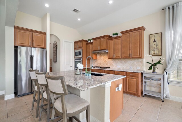 3822 Moreland Branch Ln, Katy, TX 77493 - kitchen featuring stainless steel appliances, brown cabinetry, arched walkways, decorative backsplash, and recessed lighting