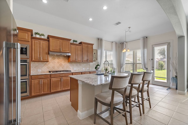 3822 Moreland Branch Ln, Katy, TX 77493 - kitchen featuring brown cabinetry, light tile patterned floors, tasteful backsplash, gas stovetop, and an island with sink