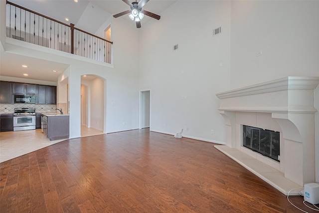 19339 Oxford Haven Dr, Cypress, TX 77433 - unfurnished living room with arched walkways, a ceiling fan, a fireplace, wood finished floors, and a high ceiling