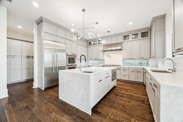 1010 Waltway Dr, Houston, TX 77008 - kitchen featuring high end appliances, wall chimney exhaust hood, a chandelier, decorative backsplash, and a center island with sink