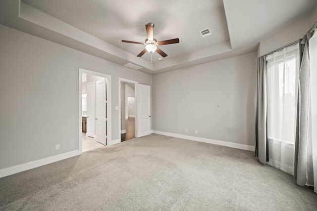 10519 Lantana Pass, Missouri City, TX 77459 - unfurnished bedroom featuring a tray ceiling, light carpet, connected bathroom, and ceiling fan