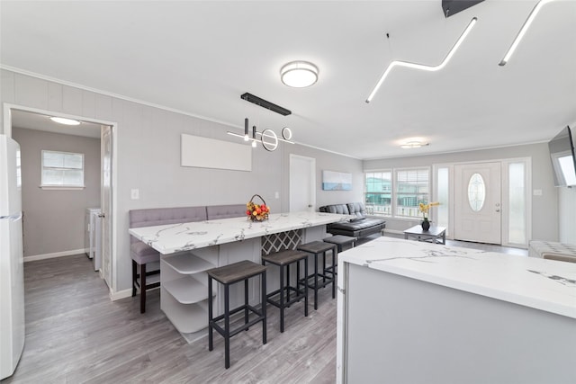 610 Seashell Dr, Freeport, TX 77541 - kitchen with crown molding, light wood-style flooring, a kitchen bar, open floor plan, and freestanding refrigerator