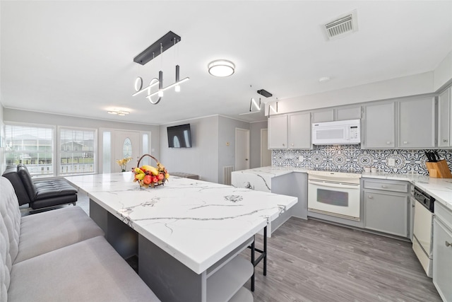 610 Seashell Dr, Freeport, TX 77541 - kitchen featuring white appliances, gray cabinetry, a kitchen breakfast bar, decorative backsplash, and light wood-style flooring