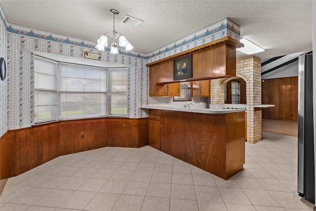 14115 Lantern Ln, Houston, TX 77015 - kitchen with a chandelier, brown cabinets, wood walls, wallpapered walls, and a peninsula