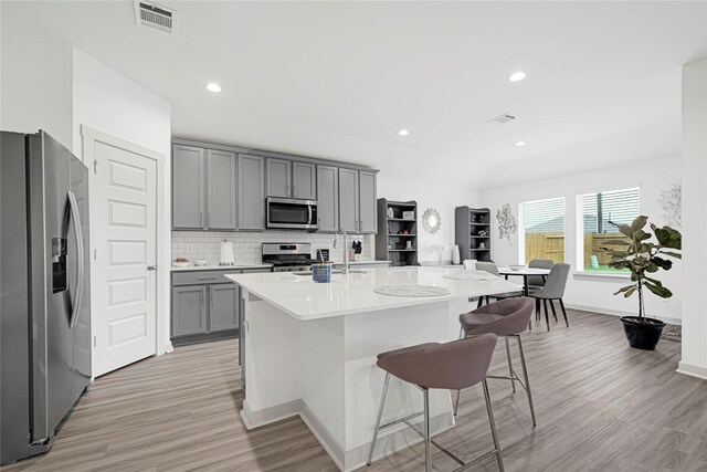 3430 Harper Meadow Ln, Missouri City, TX 77459 - kitchen with appliances with stainless steel finishes, gray cabinets, light wood-type flooring, a breakfast bar, and light countertops