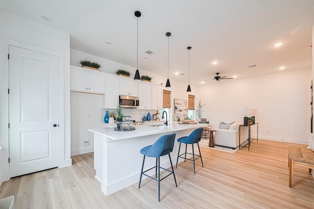 2710 Bostic St, Houston, TX 77093 - kitchen with stainless steel microwave, a ceiling fan, light wood-style flooring, white cabinets, and backsplash