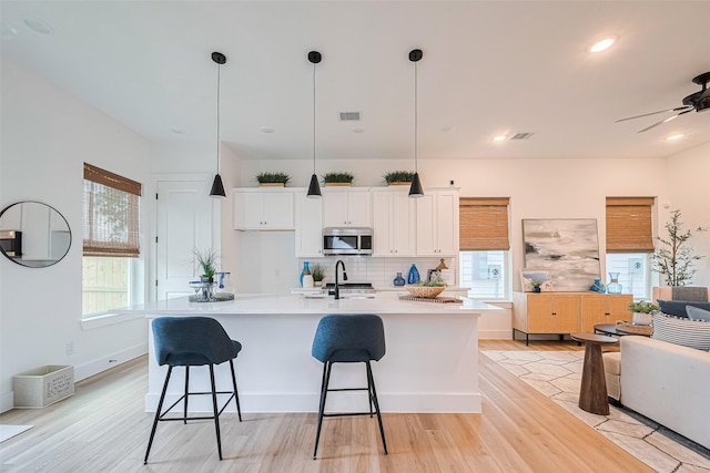 2710 Bostic St, Houston, TX 77093 - kitchen with stainless steel microwave, white cabinets, tasteful backsplash, a kitchen island with sink, and light wood finished floors