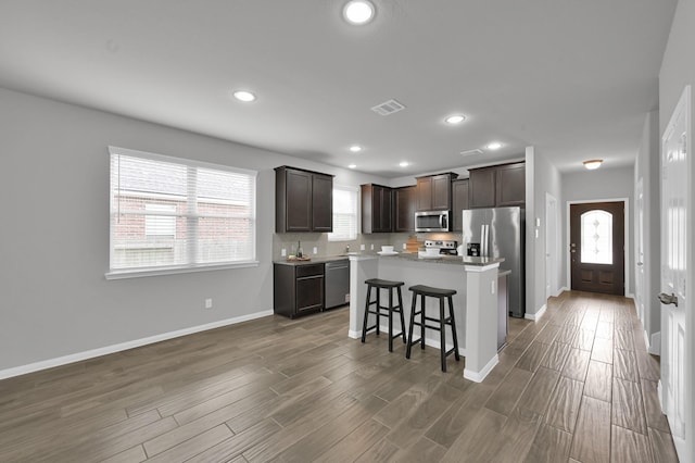 13310 Hidden Valley Dr, Montgomery, TX 77356 - kitchen with appliances with stainless steel finishes, dark brown cabinets, a breakfast bar area, a kitchen island, and wood finished floors