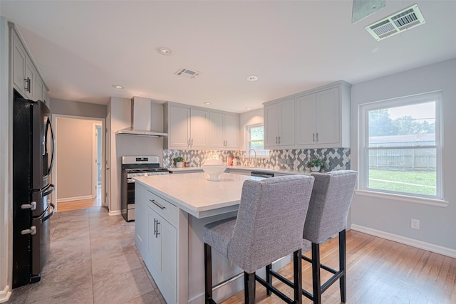 5123 Saxon Dr, Houston, TX 77092 - kitchen with wall chimney range hood, stainless steel range with gas cooktop, freestanding refrigerator, a kitchen bar, and light countertops