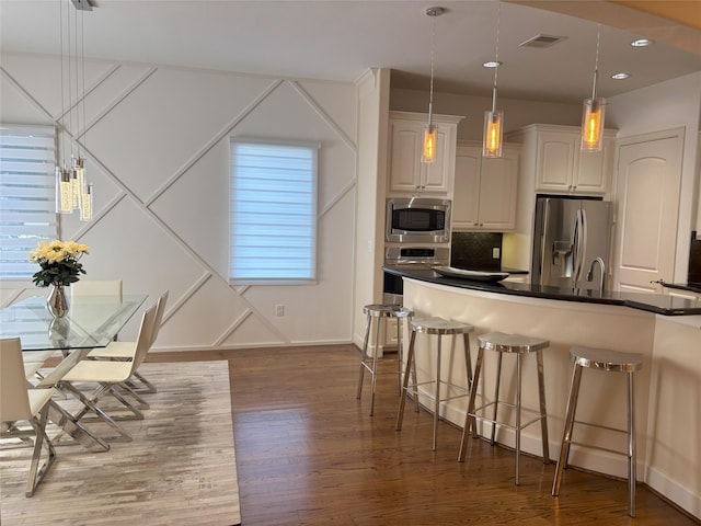 607 Oakley St Unit 5, Houston, TX 77006 - kitchen with stainless steel appliances, a breakfast bar area, wood finished floors, dark countertops, and white cabinets