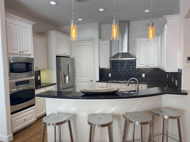 607 Oakley St Unit 5, Houston, TX 77006 - kitchen with appliances with stainless steel finishes, wall chimney exhaust hood, dark countertops, a peninsula, and a breakfast bar