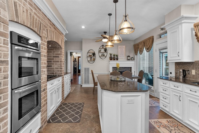 3402 Haywood Ct, Sugar Land, TX 77478 - kitchen featuring stainless steel double oven, a kitchen island, a ceiling fan, white cabinetry, and dark stone countertops