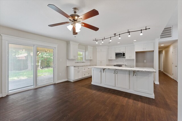 1503 Briar Cliff St, Conroe, TX 77385 - kitchen featuring stainless steel microwave, white cabinets, backsplash, track lighting, and dark wood-style flooring