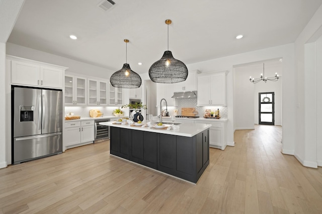 24914 Heather Glade Trl, Tomball, TX 77375 - kitchen with stainless steel fridge, under cabinet range hood, white cabinetry, light countertops, and light wood-style flooring