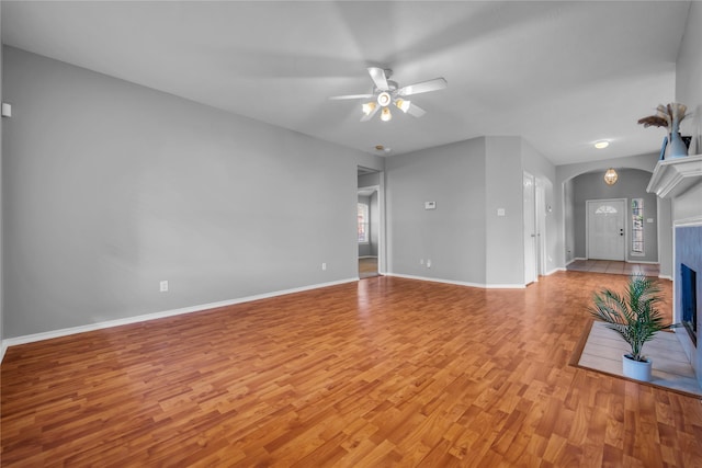 20607 Dademount Ct, Richmond, TX 77407 - unfurnished living room with light wood finished floors, a ceiling fan, a fireplace with flush hearth, and arched walkways