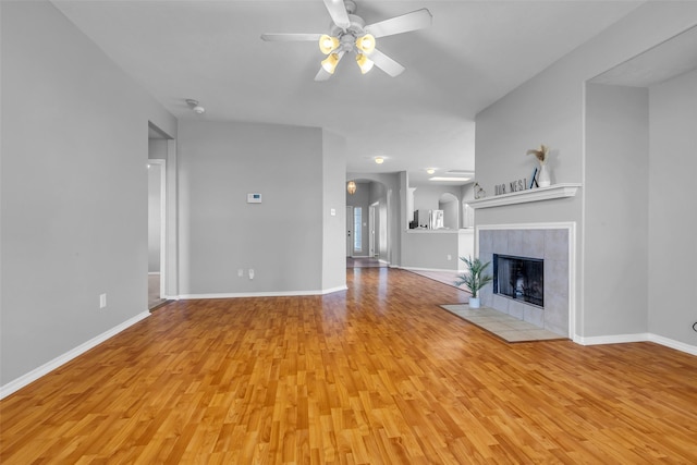 20607 Dademount Ct, Richmond, TX 77407 - unfurnished living room with light wood finished floors, a ceiling fan, a tile fireplace, and arched walkways