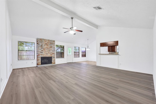 2730 Mesquite Dr, Sugar Land, TX 77479 - unfurnished living room featuring ceiling fan, beamed ceiling, light wood finished floors, a stone fireplace, and plenty of natural light