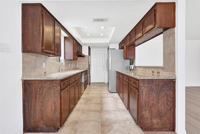 2730 Mesquite Dr, Sugar Land, TX 77479 - kitchen featuring decorative backsplash, under cabinet range hood, freestanding refrigerator, a raised ceiling, and light stone counters