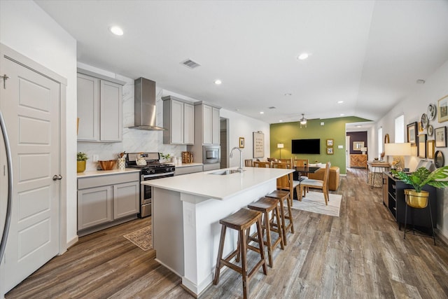 12717 Ermine St, Houston, TX 77047 - kitchen with wall chimney exhaust hood, stainless steel appliances, gray cabinets, wood finished floors, and a kitchen breakfast bar