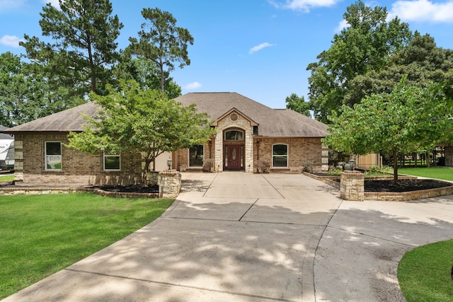 806 Garrett Dr, Magnolia, TX 77354 - french country inspired facade with roof with shingles, a front yard, brick siding, concrete driveway, and stone siding