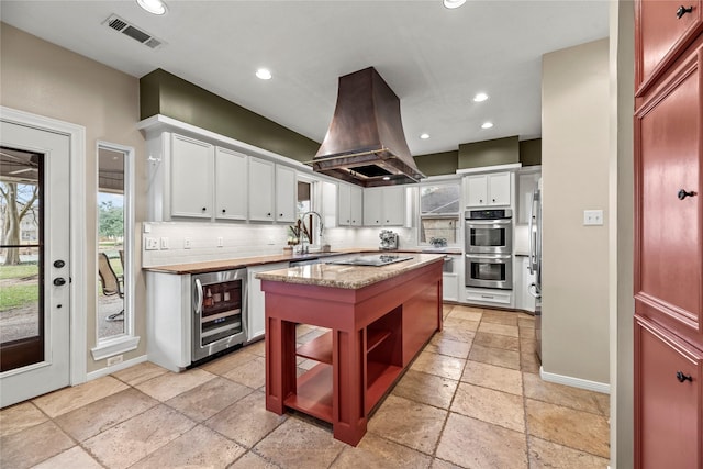 4611 Diamond Springs Dr, Missouri City, TX 77459 - kitchen featuring beverage cooler, island exhaust hood, stone tile floors, stainless steel double oven, and a center island