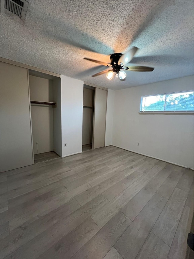 2372 Woodland Park Dr Unit 121, Houston, TX 77077 - unfurnished bedroom featuring multiple closets, light wood-style floors, a textured ceiling, and ceiling fan